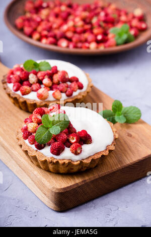 Tartelettes aux fraises sauvages avec la crème, de délicieux fruits d'été mini tartelettes sur planche à découper rustique Banque D'Images