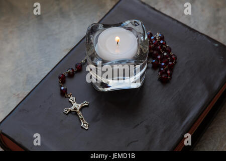 Close up of a weathered bible recouverte de cuir avec un ensemble de chapelet rouge et une bougie dans un photophore bougeoir en verre. Banque D'Images