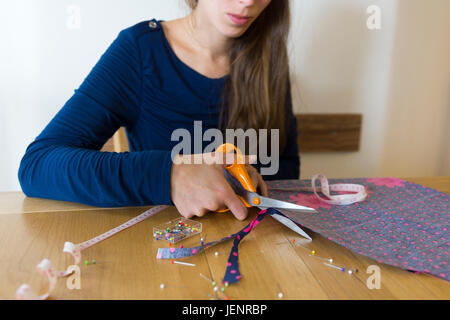 Une jeune femme coupant du matériel pour coudre une robe. Thème : passe-temps, loisirs, arts et artisanat, création, couture, broderie Banque D'Images