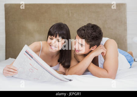Couple reading newspaper on bed Banque D'Images