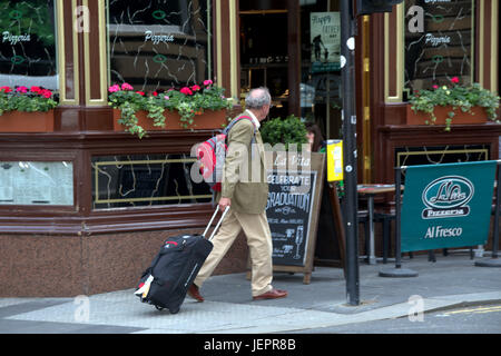 L'homme d'affaires touristique avec chariot à bagages valise à roulettes dans les rues de Glasgow crossing road à la destination ou l'hôtel Banque D'Images