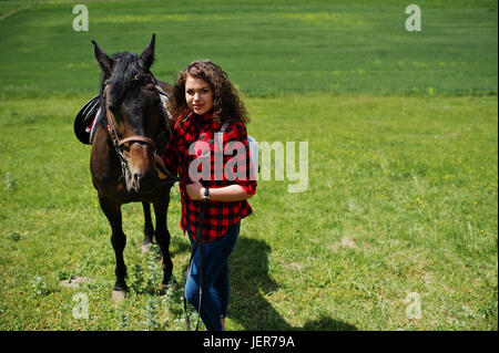 Jeune jolie fille rester à cheval sur un champ à jour ensoleillé. Banque D'Images