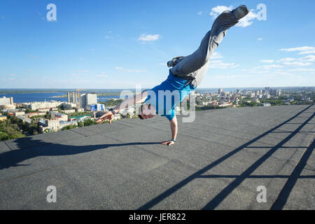 Couvreur se tient sur ses mains sur le bord du toit. Acrobaties extrêmes. Courage et de l'adrénaline. Parkour et toitures. Banque D'Images