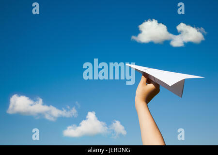 Avion en papier dans la main de l'enfant sur le ciel bleu et nuages de fond. (Avec l'espace pour le texte.) Banque D'Images