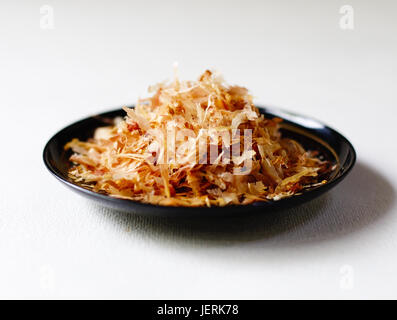 Gros plan à angle faible de katsuo bushi (bonito flakes) sur un bol noir sur un fond blanc. Banque D'Images