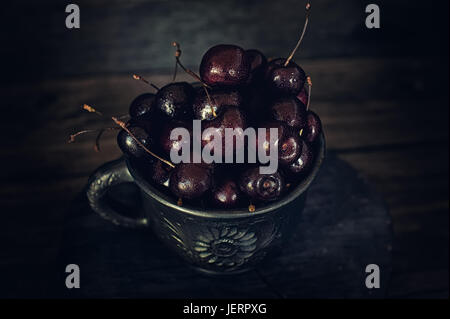 Cerises juteuses mûres avec des gouttes de rosée dans un pot en argile dans un style rustique. Banque D'Images