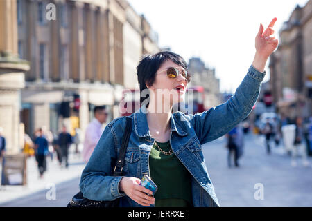 Jeune femme dans la ville. Elle est maintenant un téléphone intelligent et a la main de signal pour un taxi. Banque D'Images