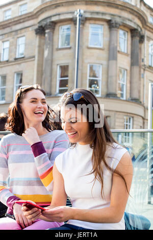 Deux femmes dans la ville. Ils sont assis sur un banc, à l'aide de smartphones. Banque D'Images