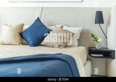 Grand lit avec oreillers et couvertures multicolores sur le mur blanc arrière-plan. Sur la droite il y a un plateau noir avec une fleur dans un vase en verre et un Banque D'Images