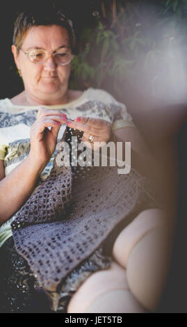 Senior woman, cheveux courts, le crochet d'une couverture marron se détendre dans le jardin. Composition verticale, se fonder sur les mains Banque D'Images