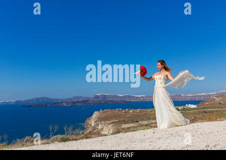 Belle femme en robe blanche se trouve près de la mer avec des fleurs Banque D'Images