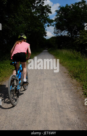 Les cycles d'une fille le long d'un chemin de terre le long d'une ligne de chemin de fer désaffectée dans le soleil de l'été Banque D'Images