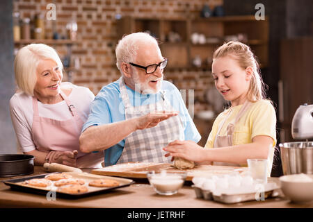 Grand-mère, grand-père et petite-fille de pétrissage et cuisson de la pâte pour les cookies à table de cuisine, la cuisson au concept de cuisine Banque D'Images