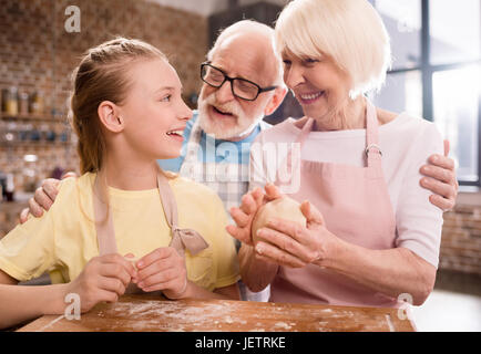 Grand-mère, grand-père et petite-fille de pétrissage et cuisson de la pâte pour les cookies à table de cuisine, la cuisson au concept de cuisine Banque D'Images