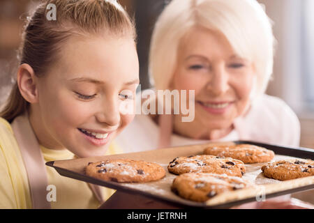 Grand-mère souriante et petit-enfant à la recherche au niveau du bac avec des cookies aux pépites de chocolat Banque D'Images