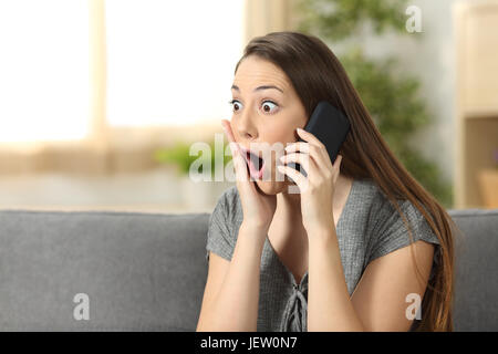 Femme dans un étonnement occasionnels appel assis sur un canapé dans le salon dans une house interior Banque D'Images