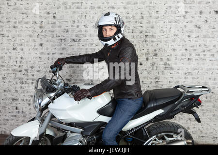 Caucasian man en veste en cuir et casque de protection assis sur le vélo dans le garage Banque D'Images