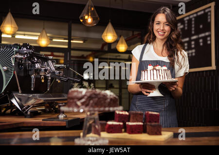 Smiling barista maintenant la plaque avec du gâteau Banque D'Images