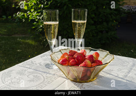 Deux verres de champagne et un bol avec des fraises sur une table avec un linge blanc dans un jardin Banque D'Images