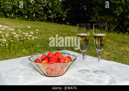 Bol avec fraises et deux verres de champagne sur une table dans un jardin verdoyant Banque D'Images