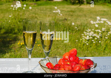 Verres de vin mousseux et un bol avec des fraises fraîches sur une table dans un jardin avec des fleurs blanches Banque D'Images