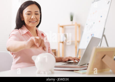 Asina positive woman putting coins en piggy bank Banque D'Images