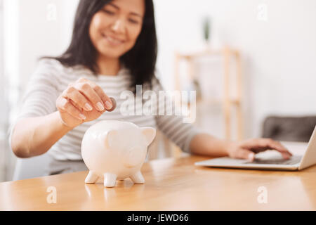 Femme positive mettre des pièces dans la tirelire Banque D'Images