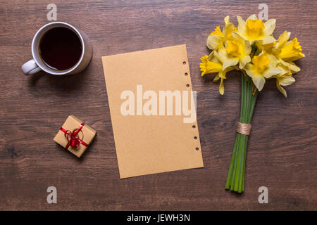 Travail avec blanc tasse de thé, un cadeau avec un ruban rouge, du papier et un bouquet de jonquilles. Banque D'Images