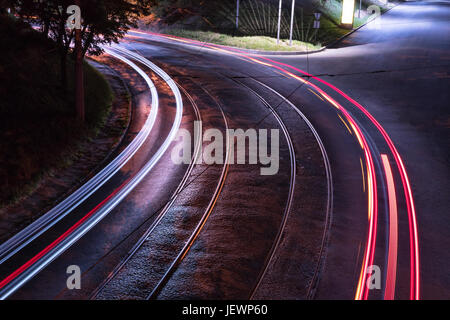 Virage de la route avec les rails du tramway à la lumière des lampes de la rue avec une trace de la lumières de voitures passant Banque D'Images