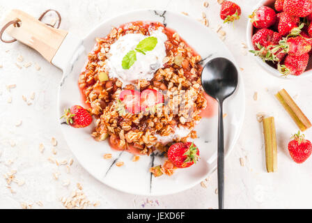 Petit déjeuner sain. Crumble d'avoine muesli avec de la rhubarbe, fraises et des mûres, les graines et la crème glacée sur la plaque de marbre blanc, à la menthe, sur Banque D'Images