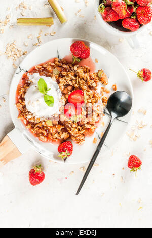 Petit déjeuner sain. Crumble d'avoine muesli avec de la rhubarbe, fraises et des mûres, les graines et la crème glacée sur la plaque de marbre blanc, à la menthe, sur Banque D'Images