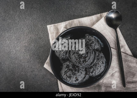 La nourriture à la mode. La glace noire avec la crème de sésame noir, noir dans un bol sur une table en pierre noire, avec une cuillère. Copy space Banque D'Images