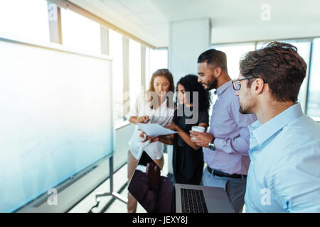 femmes d'affaires discutant un point sur le papier tandis qu'un homme travaille sur l'ordinateur. Groupe d'investisseurs hommes et femmes partageant des idées au bureau. Banque D'Images