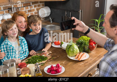 La Cuisson La cuisine en famille père prendre Photo sur Cell Smart Phone de Mère et Fils Daughter La préparation de repas sains Banque D'Images