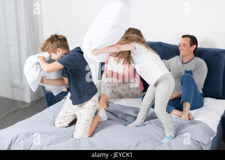 La lutte contre les oreillers, les enfants s'amuser en famille, chambre parents avec la fille et le fils ensemble joyeuse Sitting on Bed Banque D'Images