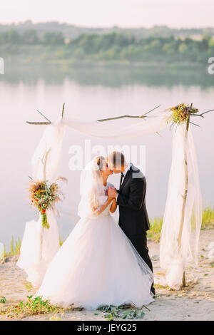 La vue verticale de l'embrassant jeunes mariés au cours de la cérémonie de mariage près de la rivière Banque D'Images