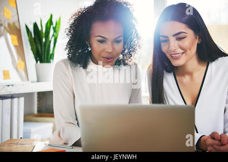 Les jeunes femmes qui travaillent ensemble sur un ordinateur portable avec l'écran de lecture heureux sourit, sun flare derrière Banque D'Images