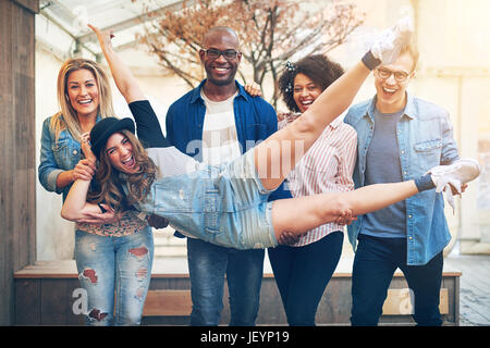 Noir et blanc expressif friends holding cheerful woman lying on leurs mains et rire ensemble. Banque D'Images