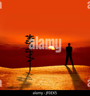 La silhouette de l'image conceptuelle signe directionnel et homme d'affaires sur le coucher du soleil sur le paysage sec craquelé Banque D'Images