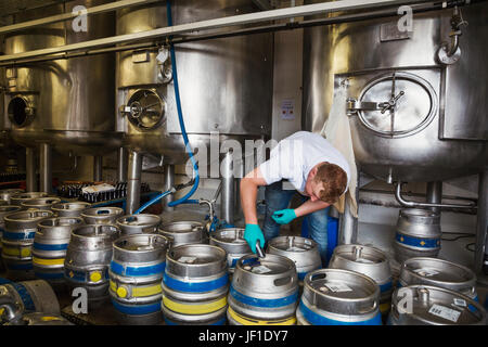 Homme travaillant dans une brasserie, la fermeture des fûts de bière en métal. Banque D'Images