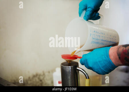 Personne portant des gants en latex bleu verser un liquide brun à partir d'un pot en plastique à travers un filtre dans une brasserie. Banque D'Images