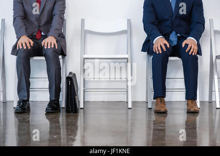 Les hommes d'affaires en costumes assis sur des chaises blanches en salle d'attente, réunion d'affaires. Banque D'Images