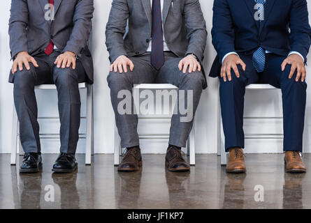 Les hommes d'affaires en costumes assis sur des chaises blanches en salle d'attente, réunion d'affaires. Banque D'Images