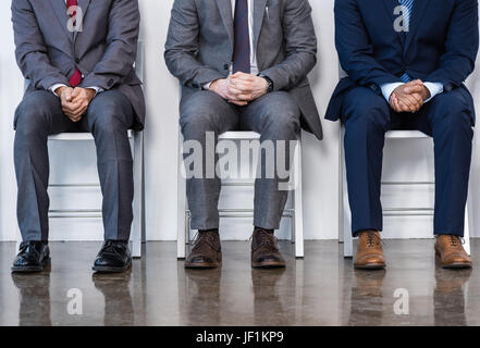 Les hommes d'affaires en costumes assis sur des chaises blanches en salle d'attente, réunion d'affaires. Banque D'Images