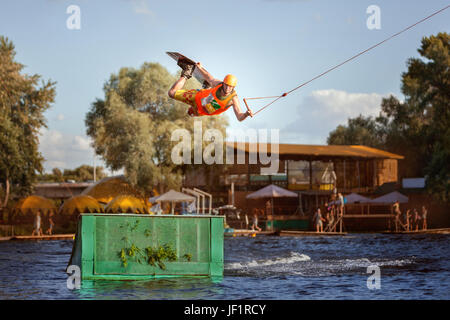 Skateboarder mâle saute par dessus un tremplin sur un lac, c'est un sportif extrême. Banque D'Images