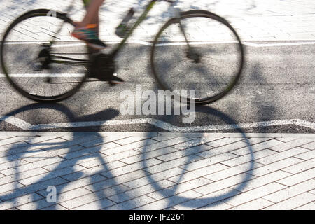 Cycliste et silhouette floue ombre sur une piste cyclable asphaltée à côté de trottoirs pour piétons Banque D'Images