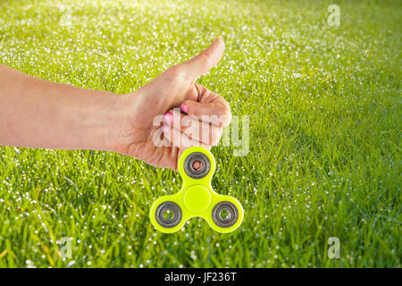 Femme hand holding yellow fidget spinner with Thumbs up sur un fond ensoleillé Banque D'Images