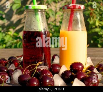 Le jus de cerise et d'orange en bouteille froide avec le tube sur une table en bois. Banque D'Images