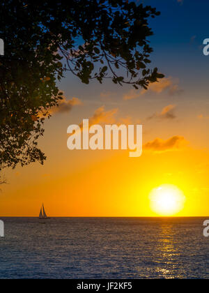 Le soleil se couche comme un petit Yacht passe au large de la côte de Mustique, vu de l'Cotton House Beach Banque D'Images