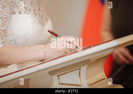 Mariée met sa signature dans le livre d'enregistrement de plume du mariage. Banque D'Images